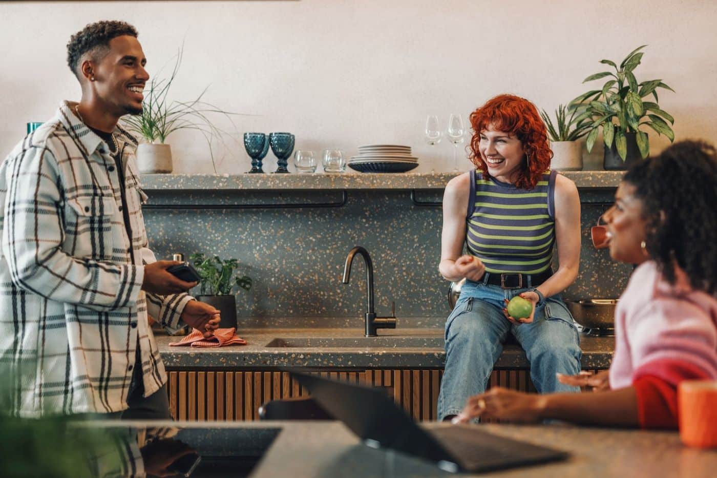 Three friends talking and eating in a kitchen